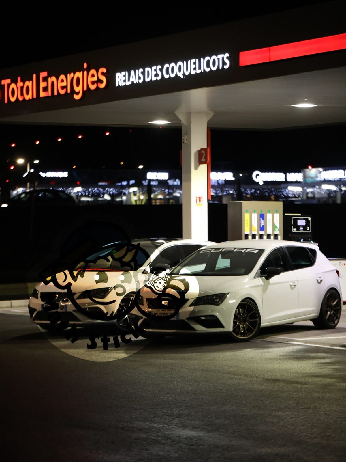 Cupra Leon blanche avec bandeau pare-brise personnalisé, de nuit devant une station-service